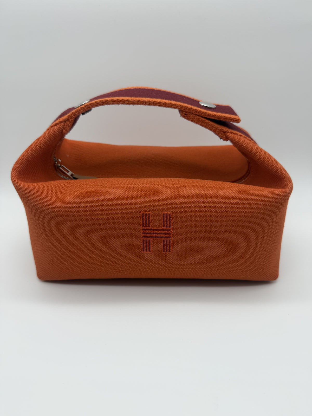 Hermès Bride-A-Brac PM in orange canvas, front view with the embroidered H and the bordeaux strap fastened over the top