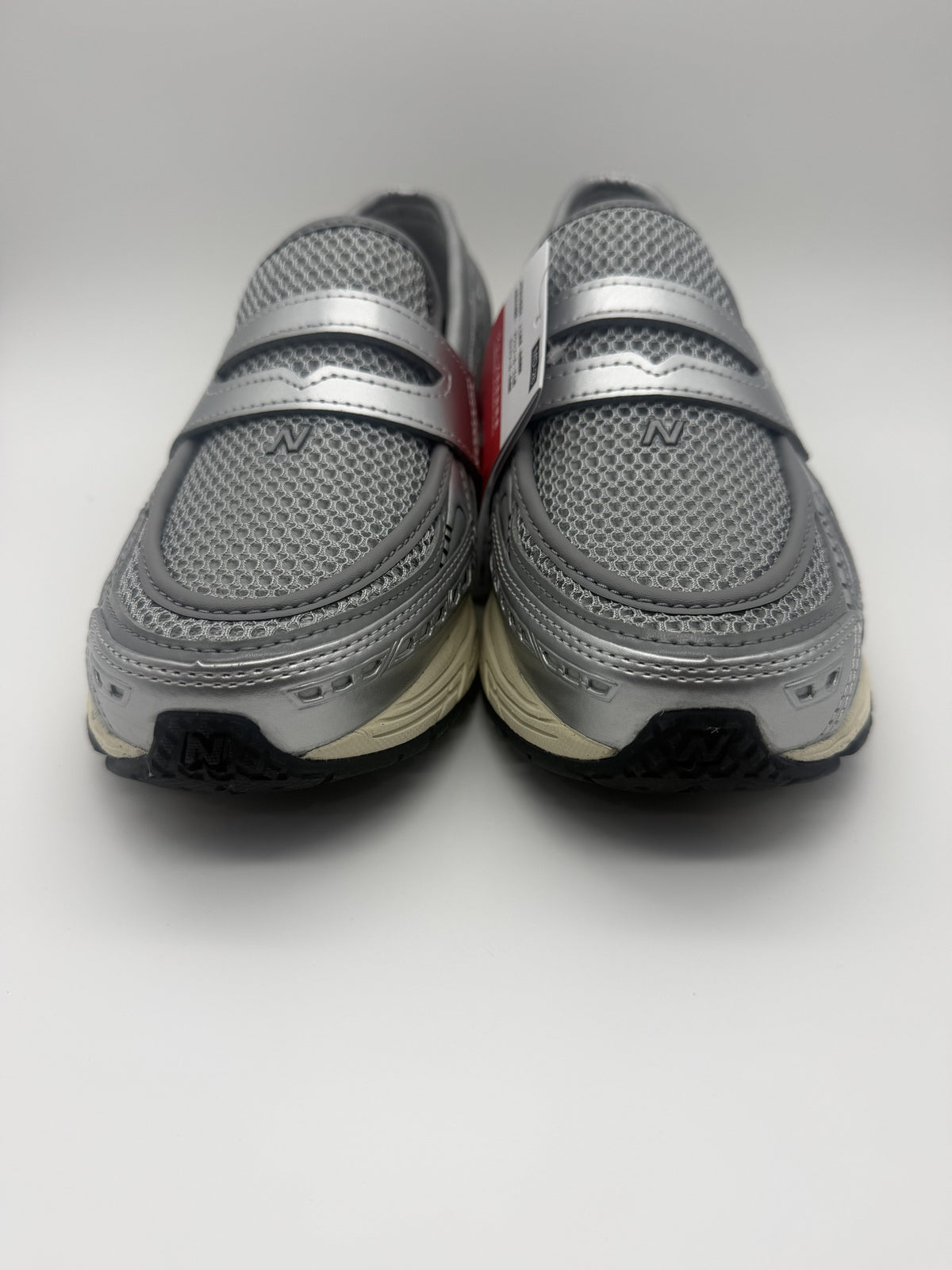 Front view of both loafers with the New Balance hangtag attached, showing the toe bumpers and midsoles