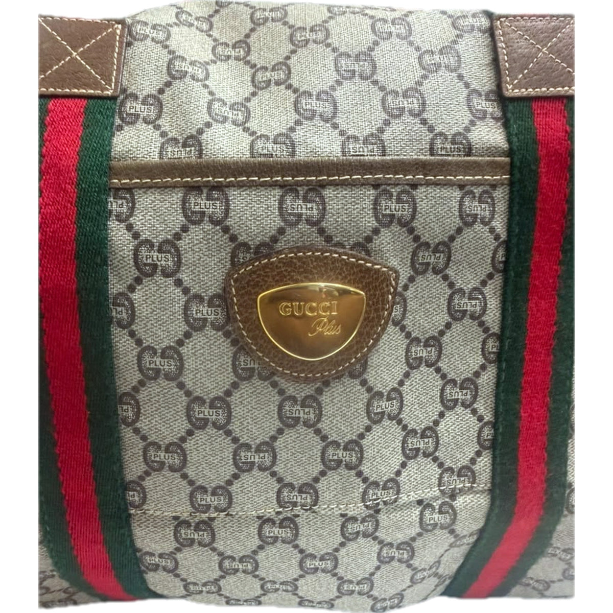 Close view of the gold-tone GUCCI Plus shield plaque on its pebbled leather mount